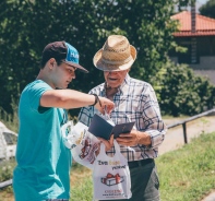 Jugendlicher berreicht einem lteren Griechen ein Bibelpckchen.