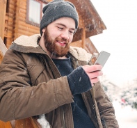 Warm gekleideter Mann mit Bart schaut lchelnd auf sein Handy