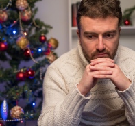 Deprimierter Mann vor Weihnachtsbaum