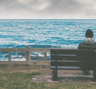 Mann sitzt auf der Bank mit Blick aufs Meer.