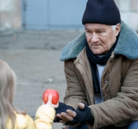 Mdchen reicht Obdachlosem einen Apfel