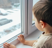 Warten auf eine Familie. Junge blickt traurig aus dem Fenster (Symbolbild).