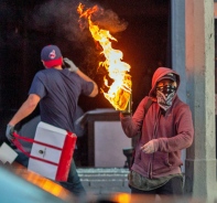 Eine Person wirft einen Molotow-Cocktail, whrend eine andere Person ein Geschft plndert