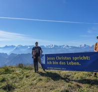 Mit einem grossen Bibelvers-Plakat in den Bergen